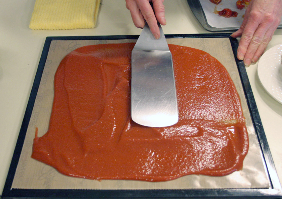 Orange fruit puree being spread on a silicone mat with a spatula to make fruit leather