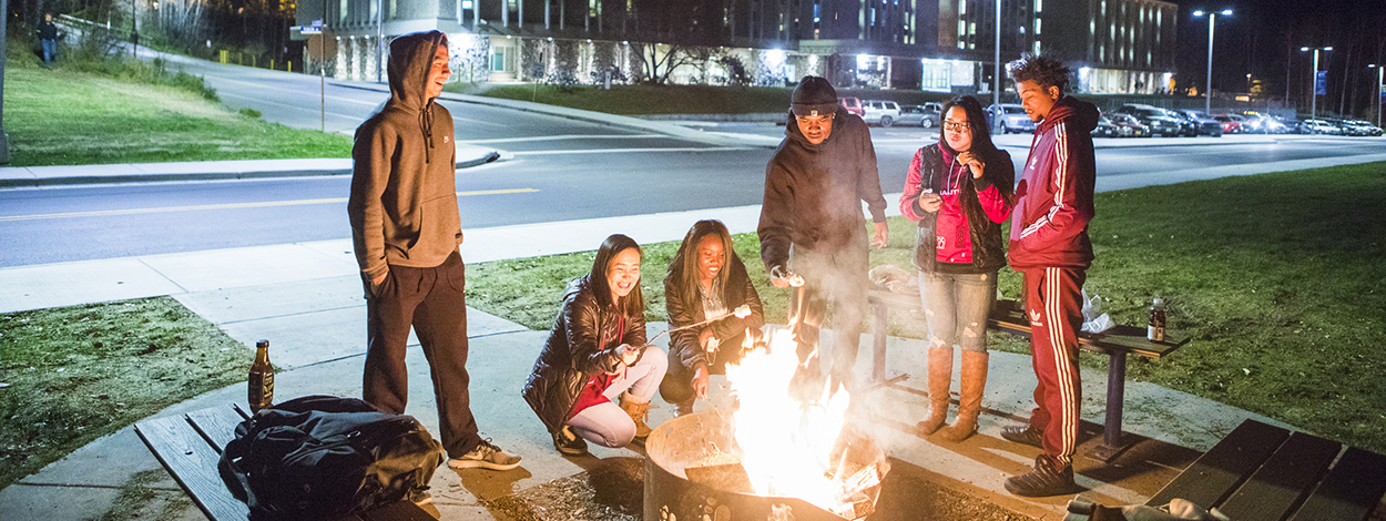 Ͷע students roast marshmallows around a fire pit on campus
